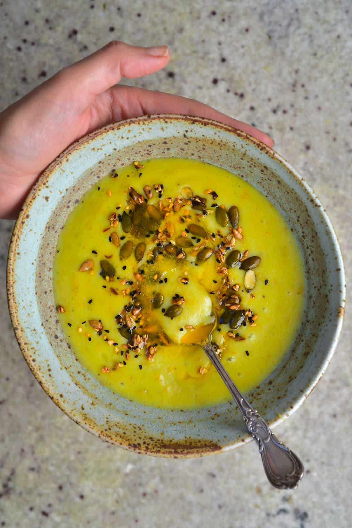 A bowl with potato leek cram soup topped with seeds and a spoon dipped in it