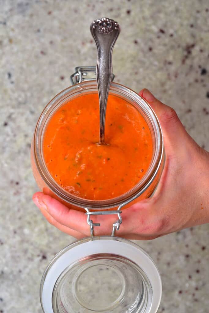 A jar with roasted red tomato sauce and a spoon dipped in it
