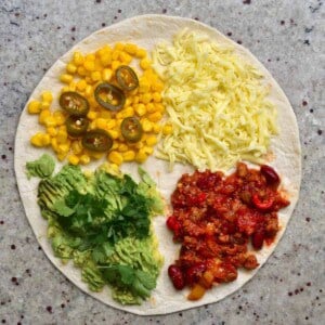 A tortilla topped with cheese, corn, jalapeños, avocado, vegan chili con carne