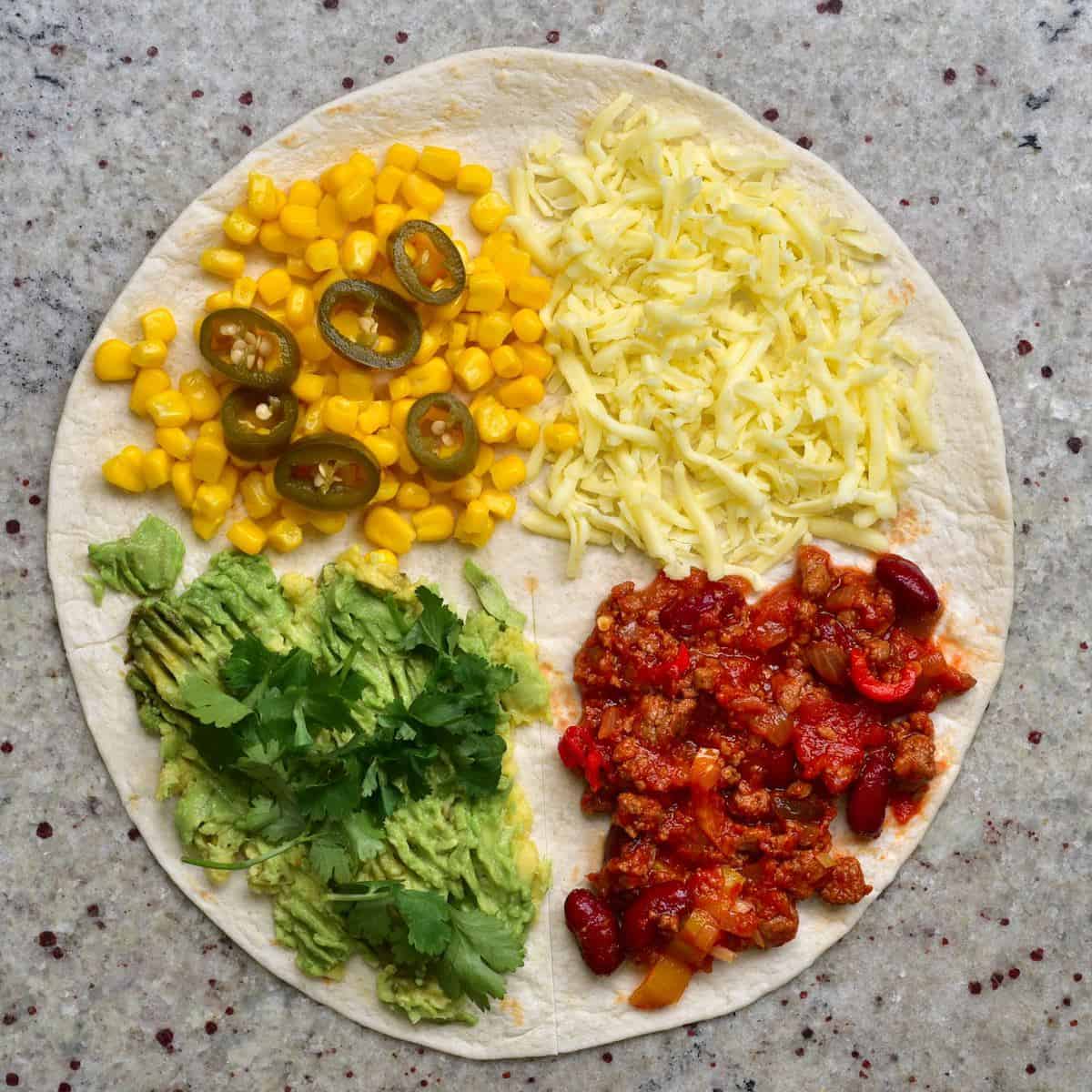 A tortilla topped with cheese, corn, jalapeños, avocado, vegan chili con carne