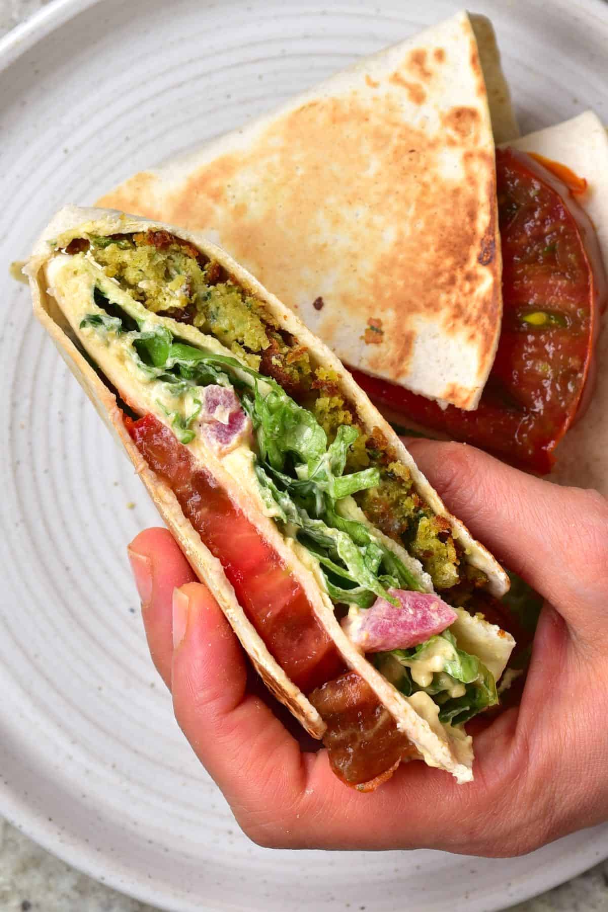 Falafel tortilla with tomato and lettuce held in a hand