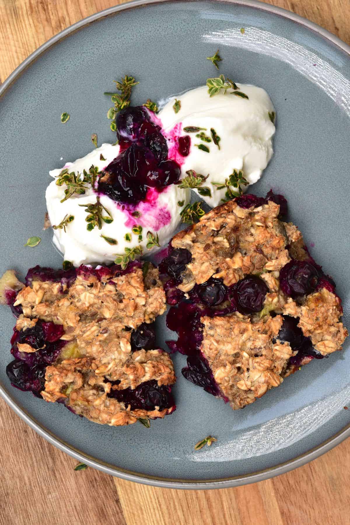 Two squares of baked blueberry oats served with yogurt