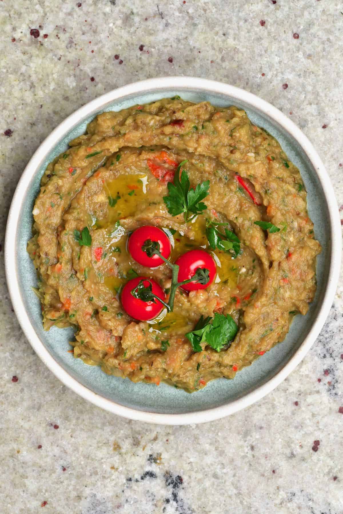 A bowl with Caribbean eggplant dip topped with three cherry tomatoes and cilantro