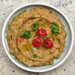 A bowl with Caribbean eggplant dip topped with three cherry tomatoes and cilantro