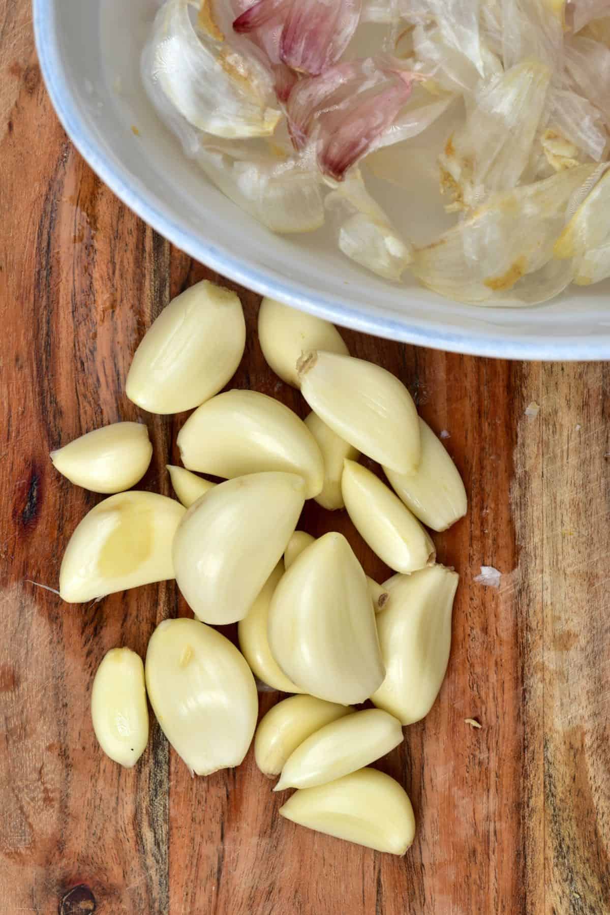 A few peeled garlic cloves next to a bowl with their peels