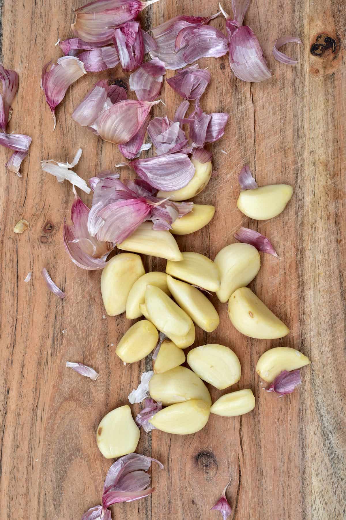 Some peeled garlic cloves and peels on a wooden board