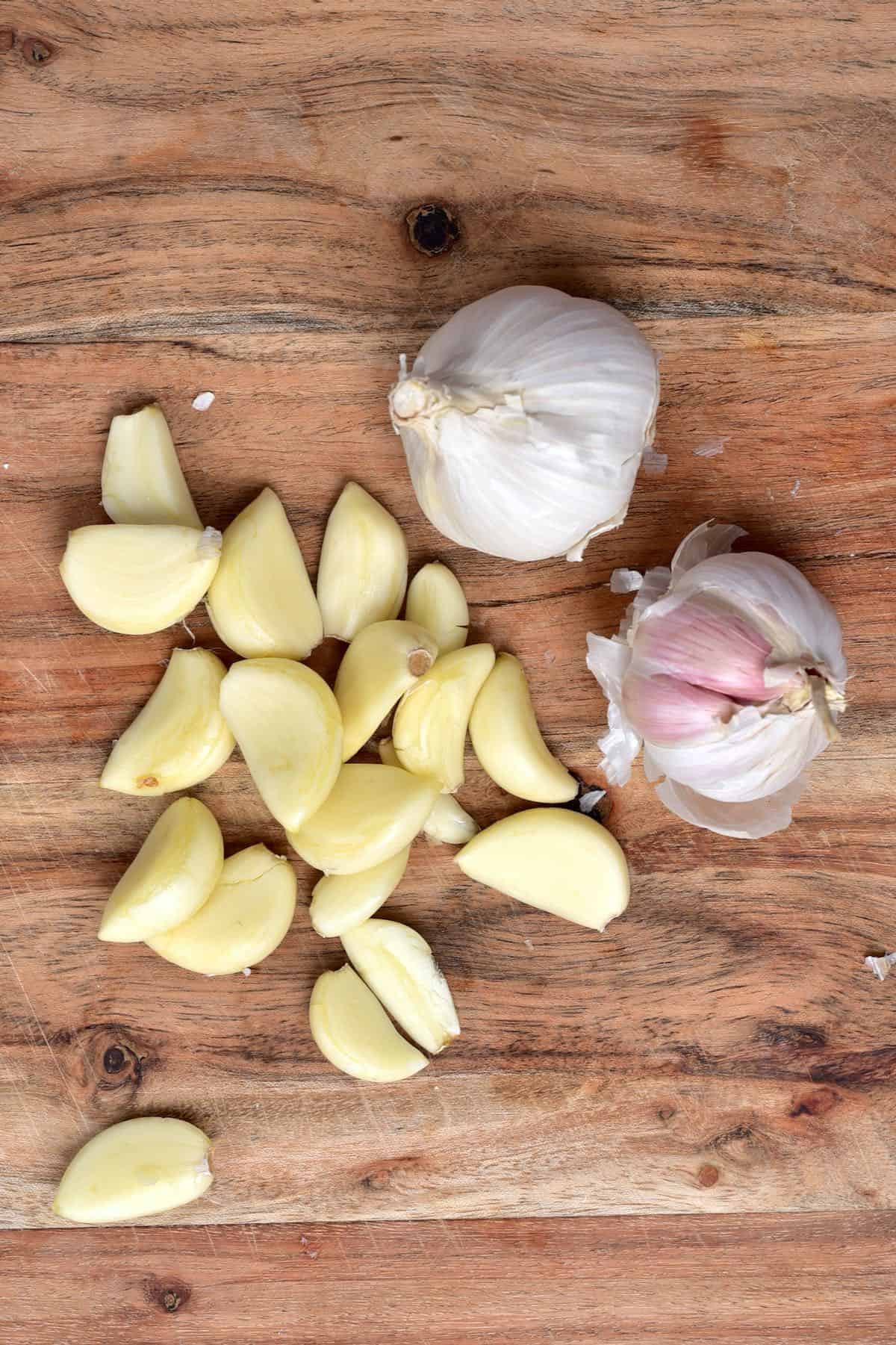 Some peeled garlic cloves and two garlic heads on a wooden board