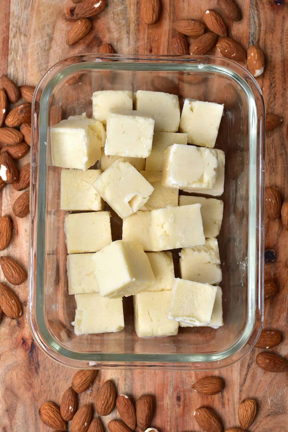 Almond butter ice cubes in a container and some almonds around it