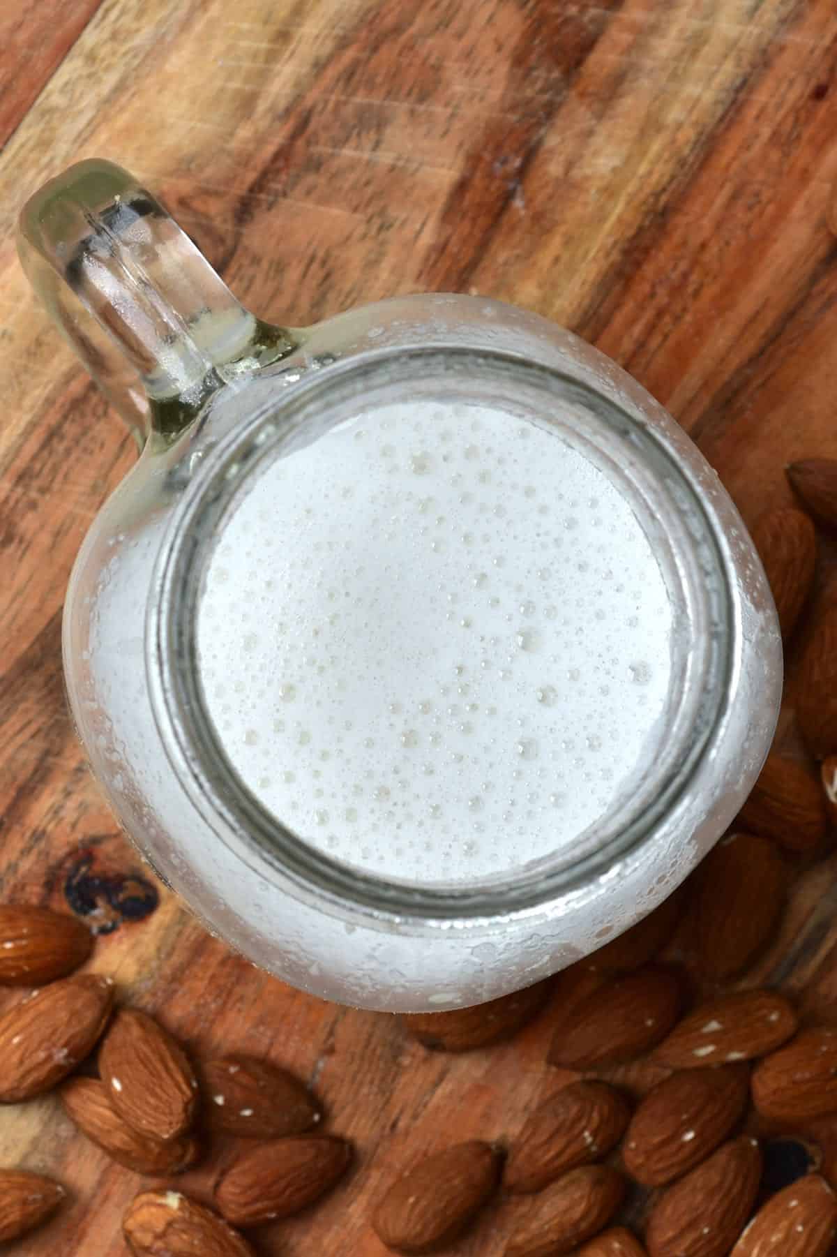 A glass with almond milk and some almonds around it