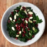 A bowl of kale salad topped with slivered almonds and pomegranate seeds
