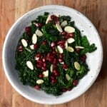 A bowl of kale salad topped with slivered almonds and pomegranate seeds - 17