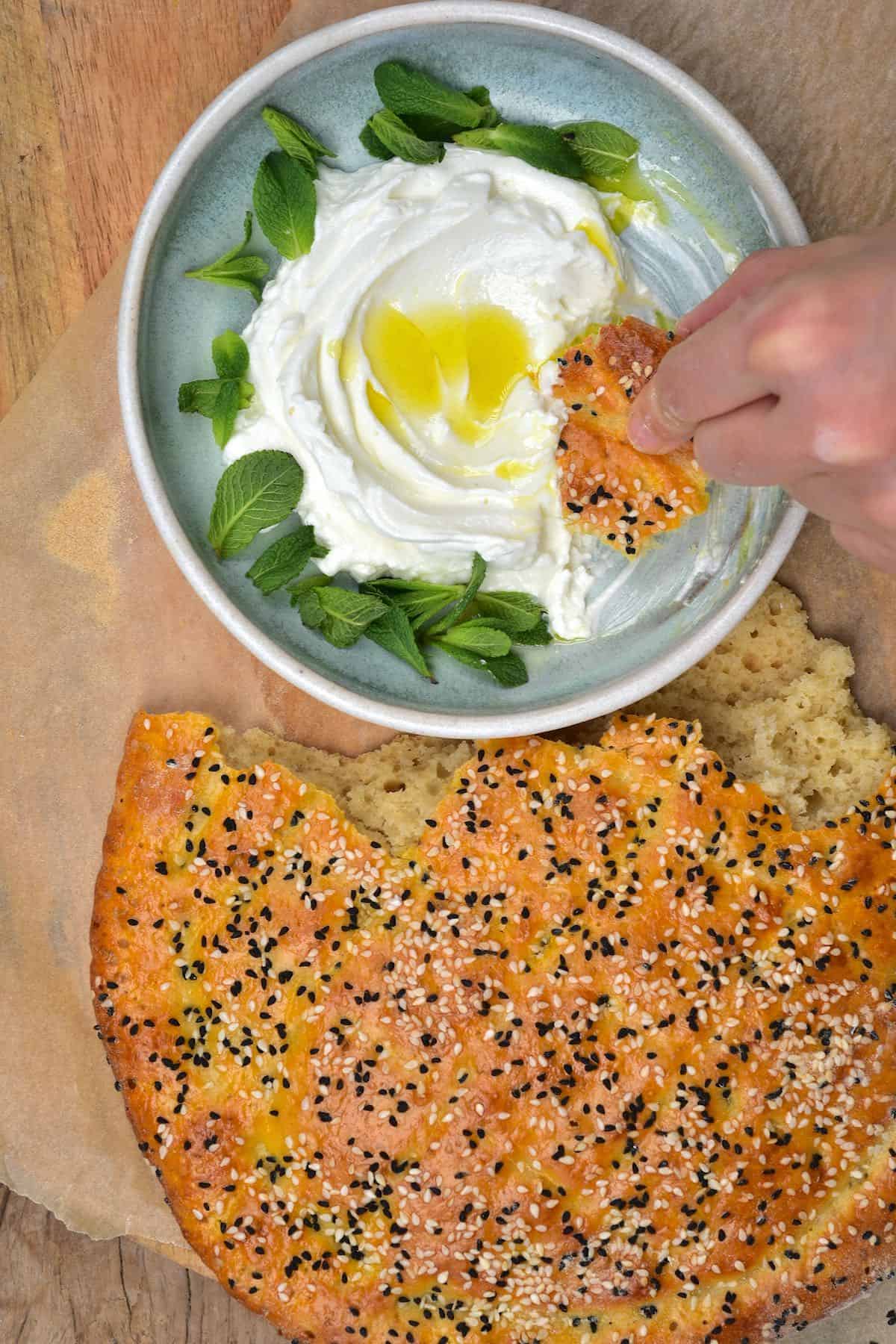 Pide bread and a bowl with labneh with a piece of bread being dipped in it