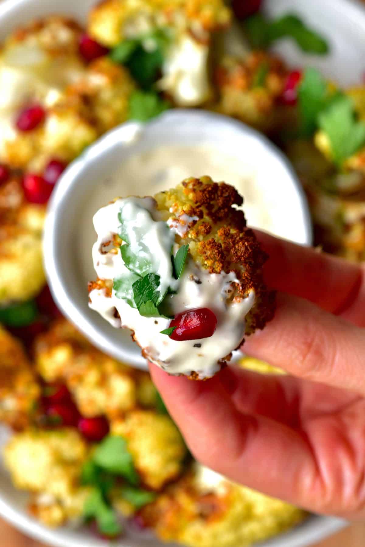 air fried cauliflower floret dipped in tahini sauce and topped with parsley and pomegranate seed