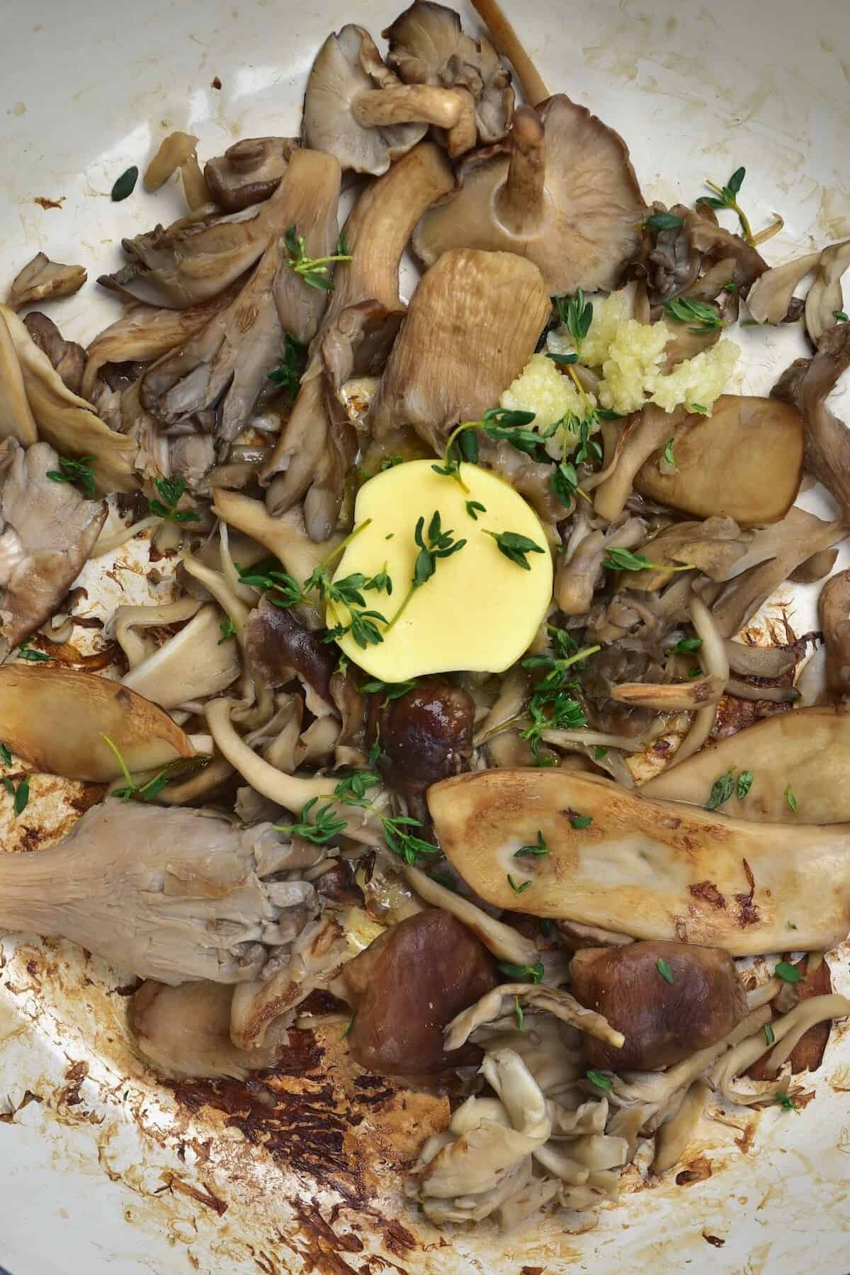 Adding butter and herbs to cooking mushrooms