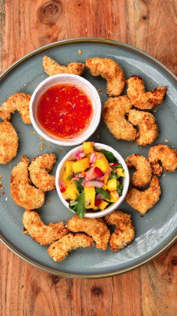 A plate with crispy baked shrimp and two small bowls with chili sauce and mango salsa