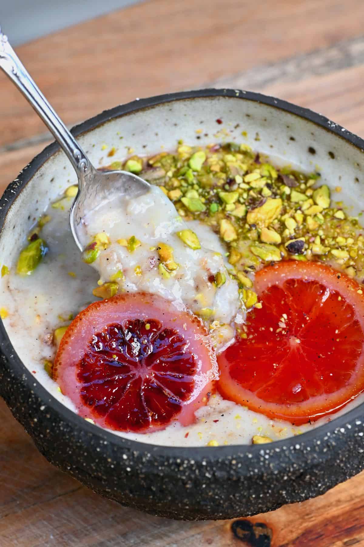 Banana oatmeal in a bowl topped with pistachios and orange slices