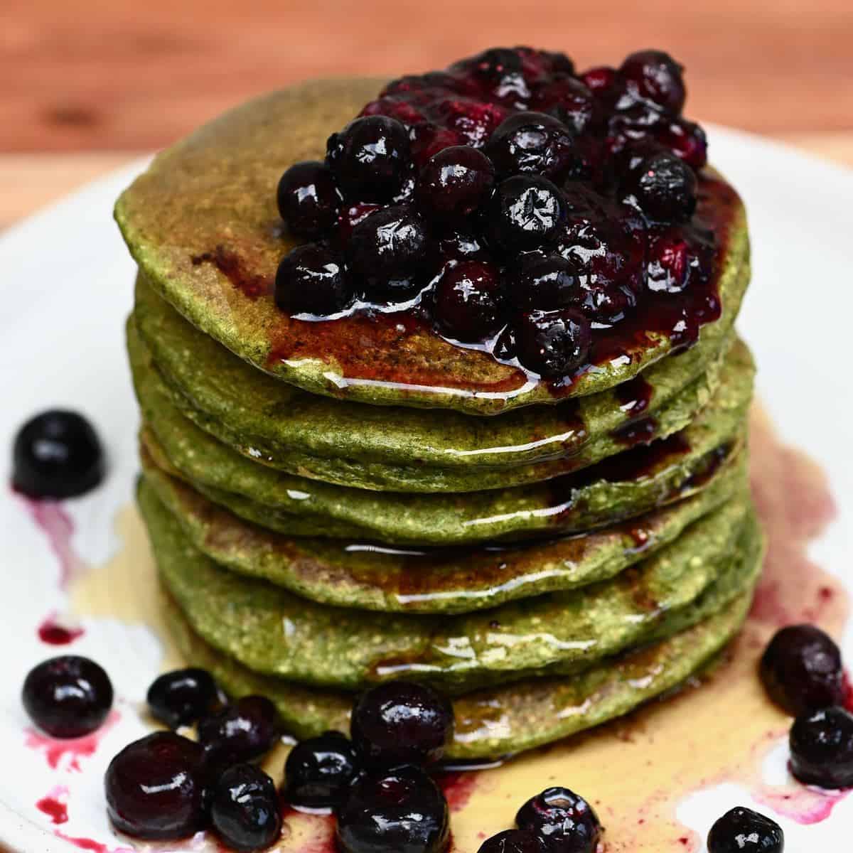A stack of green spinach pancakes topped with berry compote