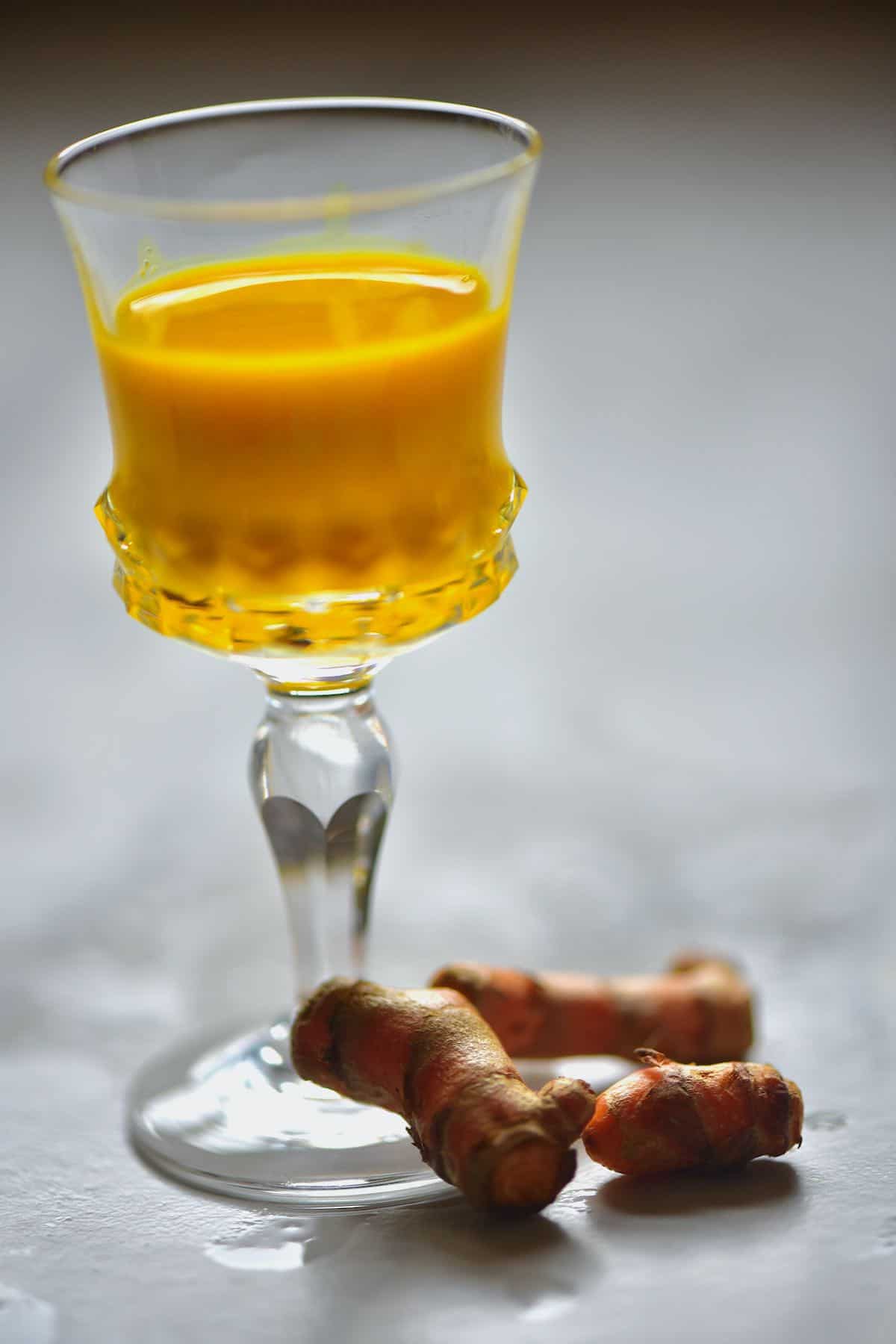 A small glass with turmeric juice and turmeric next to it