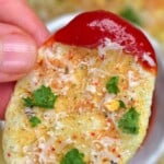 A potato chip topped with parmesan dipped in ketchup