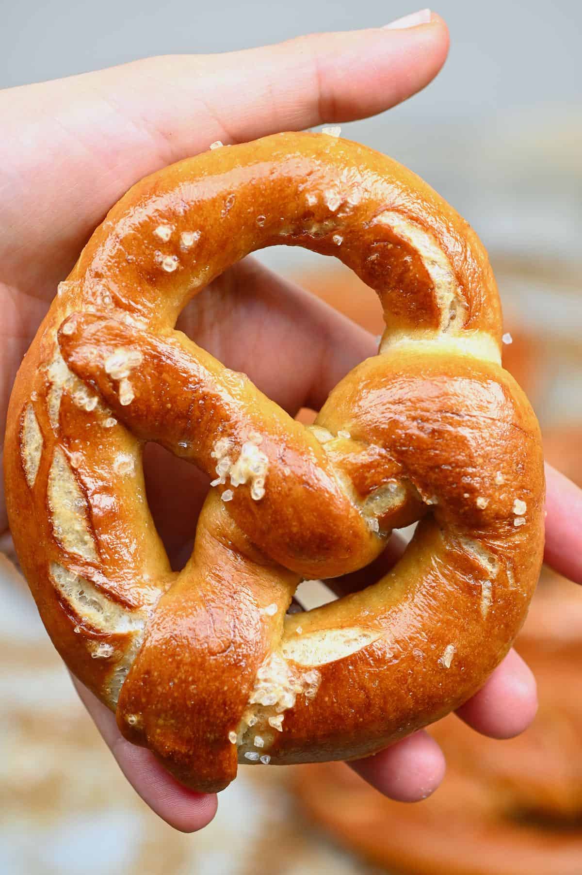 A hand holding a homemade pretzel topped with coarse salt