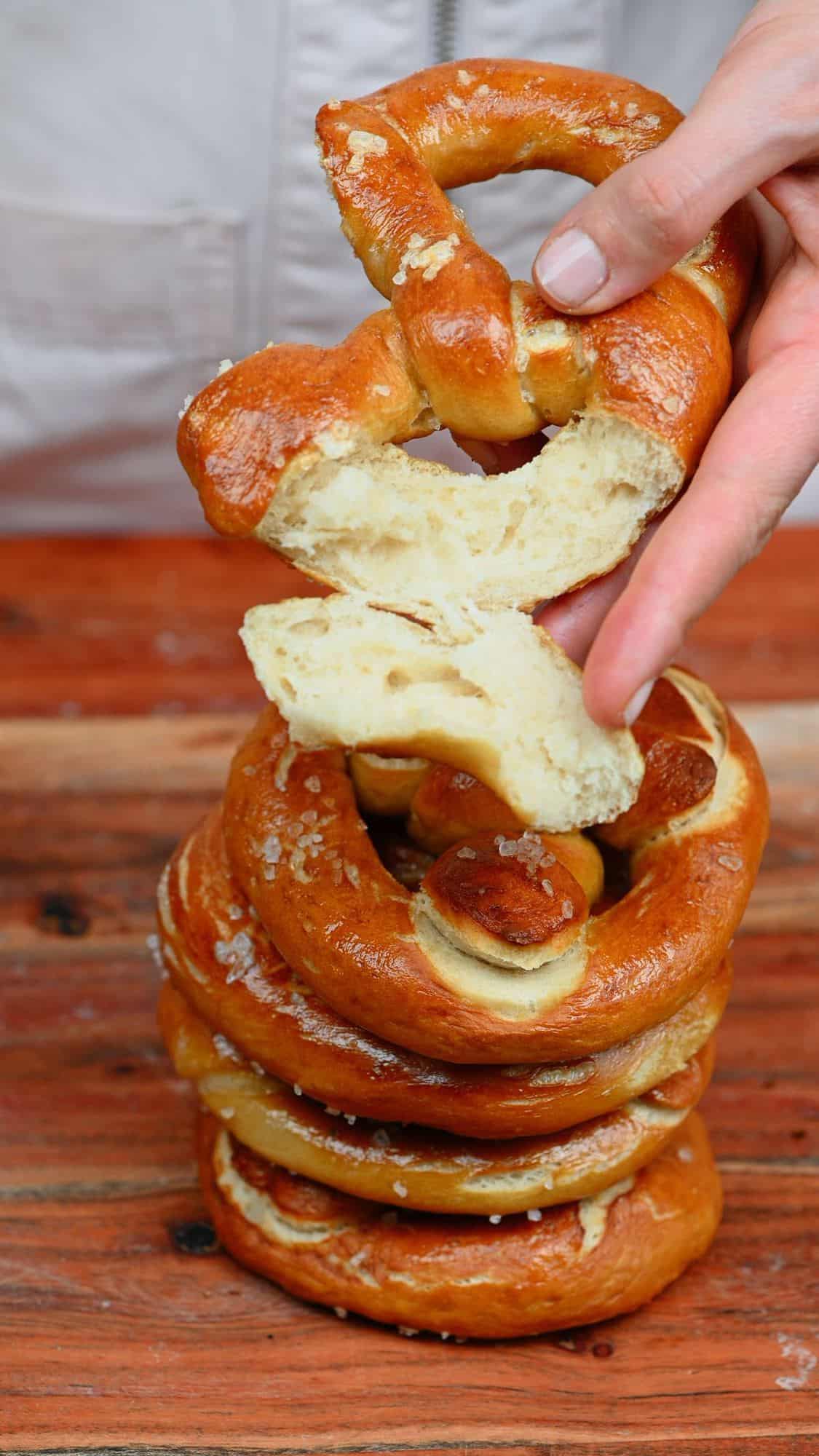 A hand holding pretzel with a piece cut off and a stack of four pretzels underneath