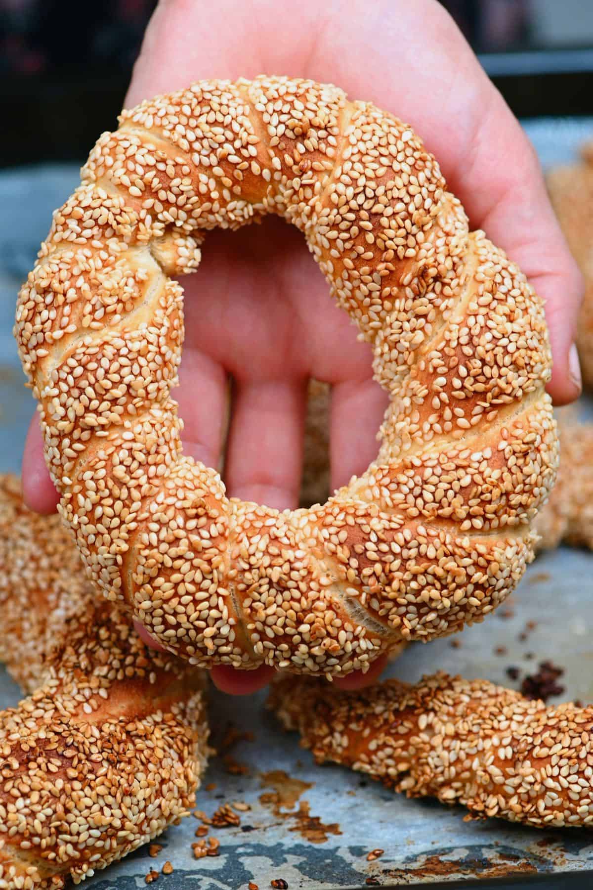 A hand holding a baked simit