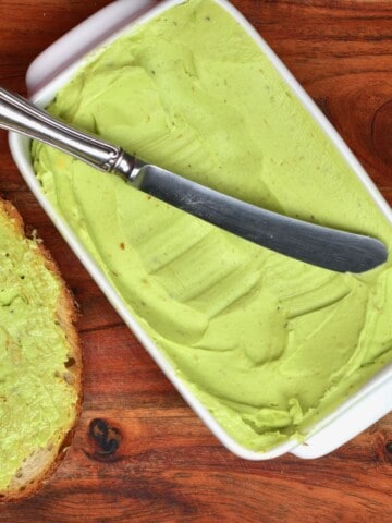 Avocado butter in a butter dish with a knife and toast on the side