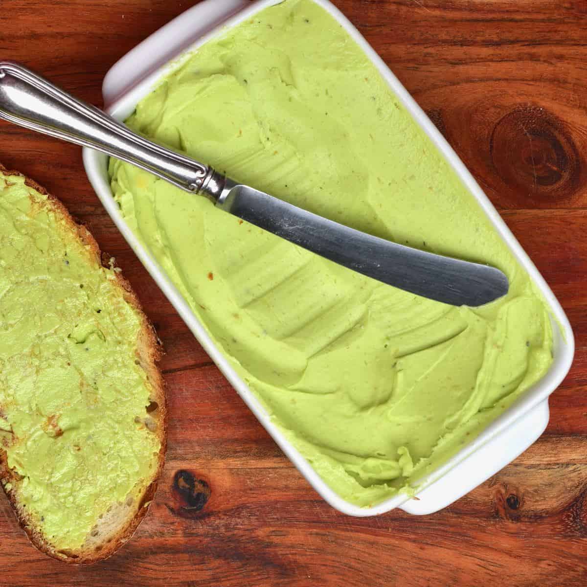Avocado butter in a butter dish with a knife and toast on the side