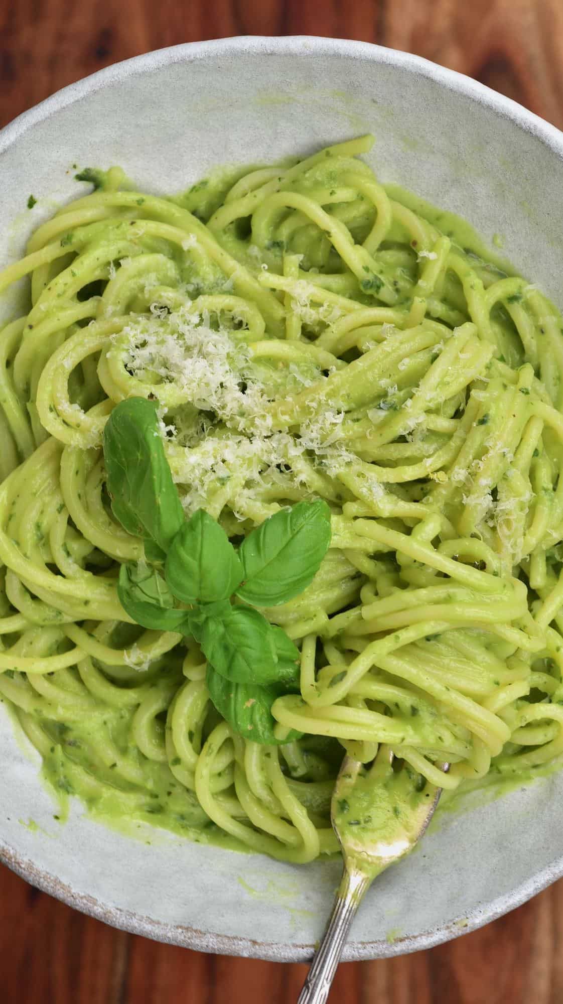 Avocado pasta in a bowl topped with parmesan and basil leaves