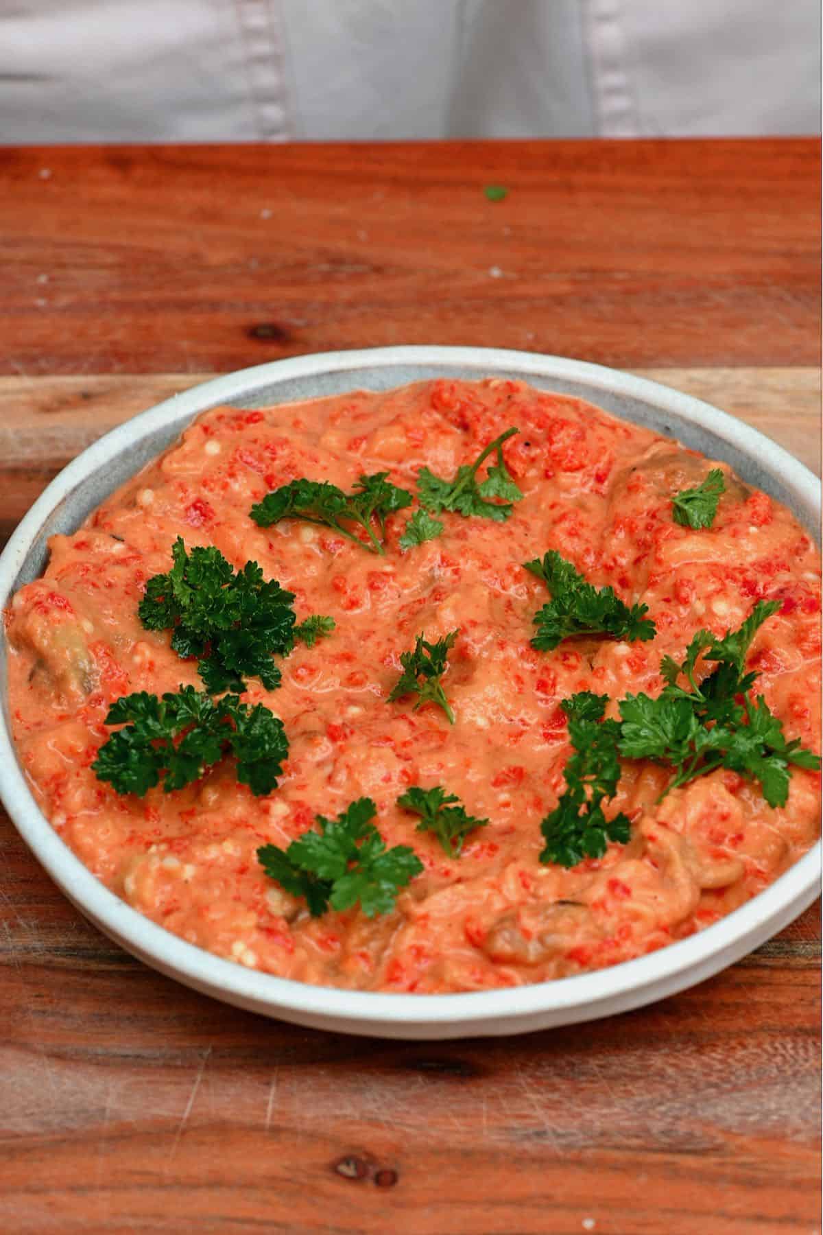 A bowl with roasted pepper eggplant dip topped with parsley