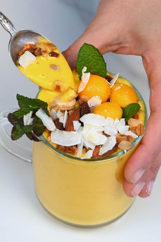 A cup with mango lassi topped with granola