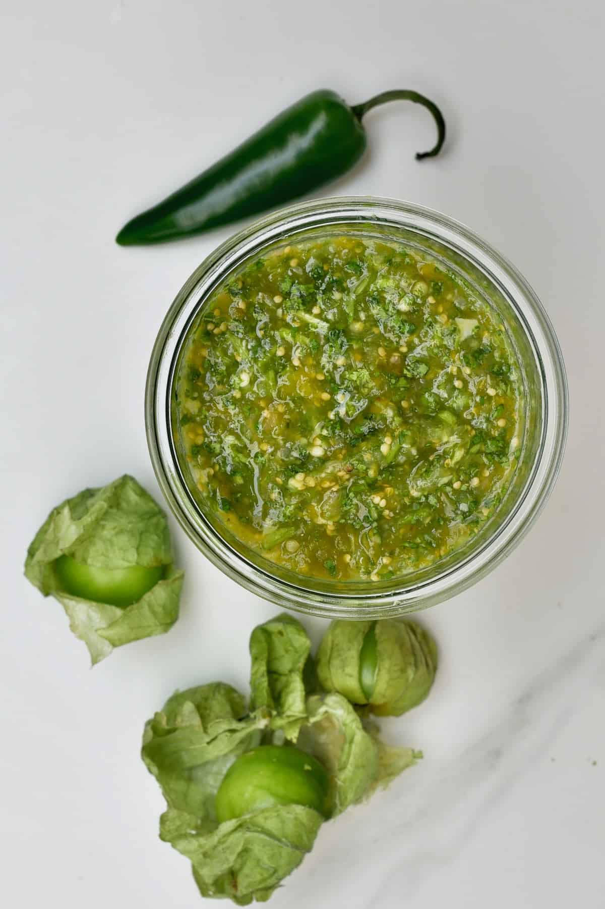 Salsa verde (tomatillo green chili salsa) in a jar with tomatillo and jalapeño next to it