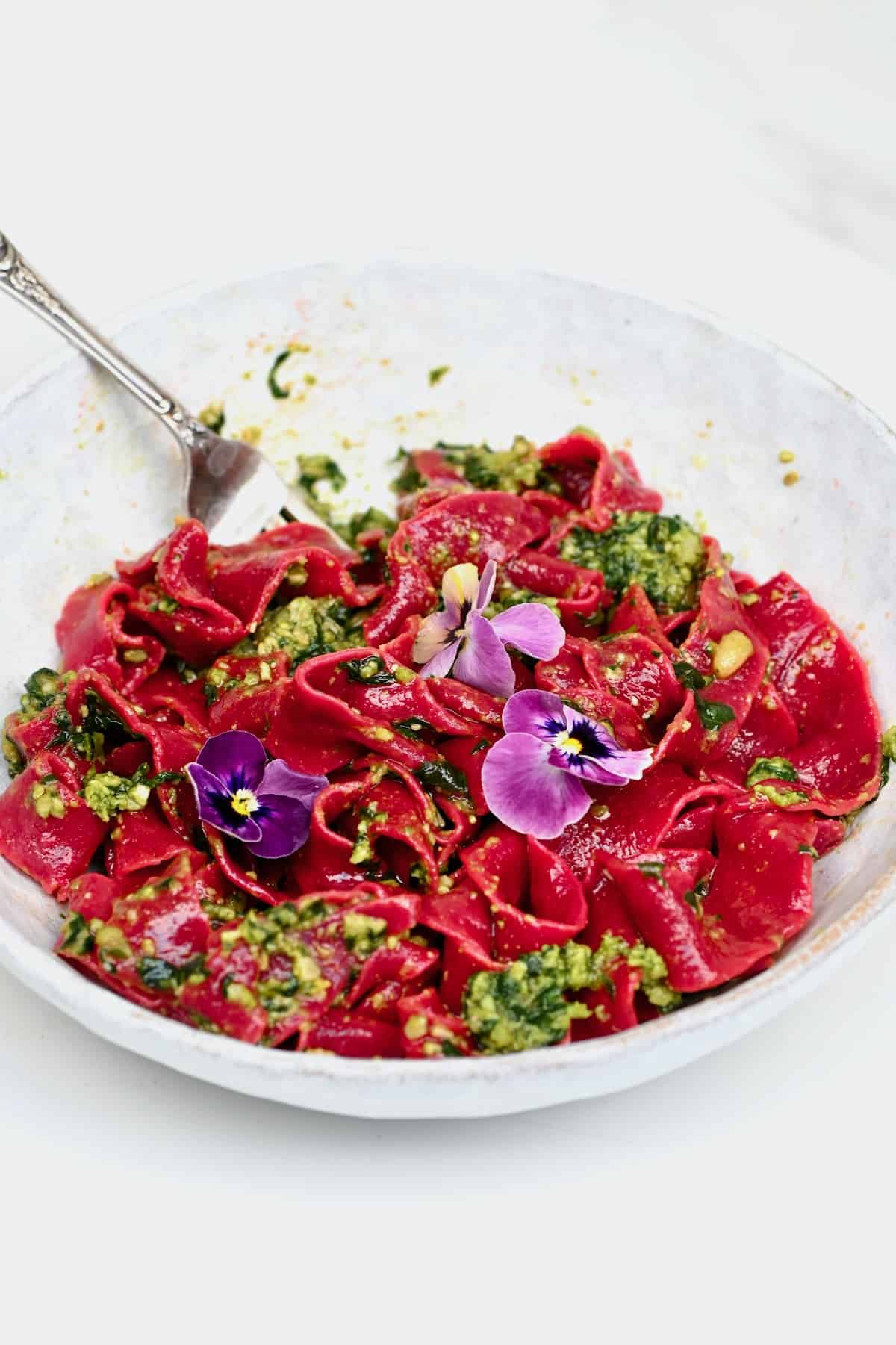 A serving of beetroot pasta basil pesto and flower decoration