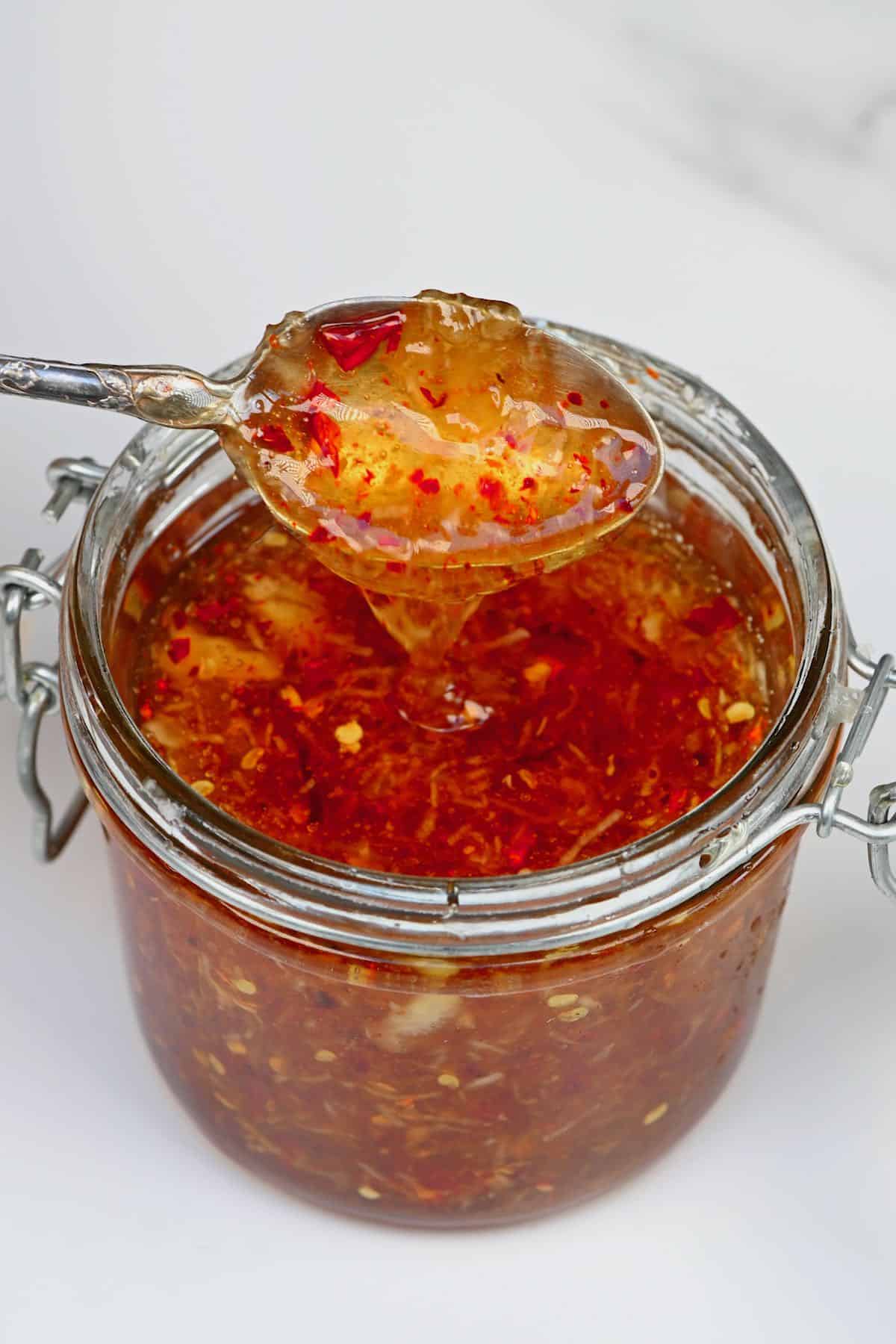 A spoonful of garlic chili honey dripping over a jar