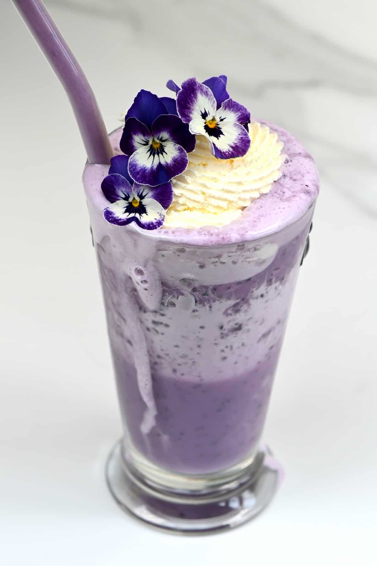 Blueberry ube shake with a straw and decorated with edible flowers