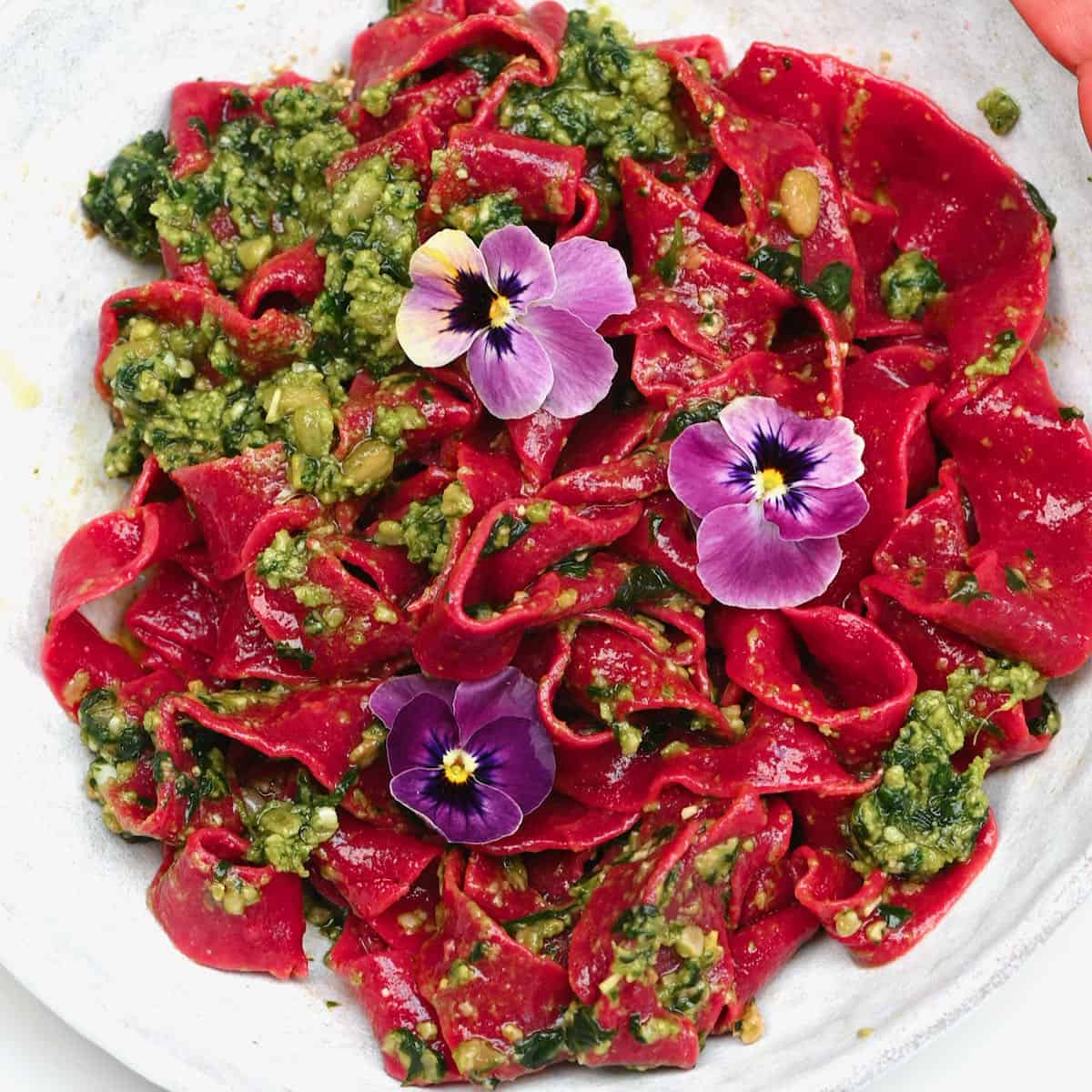 Pink beet pasta topped with pesto and edible flowers