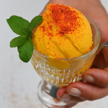 Mango ice cream serving topped with tajin and mint leaves