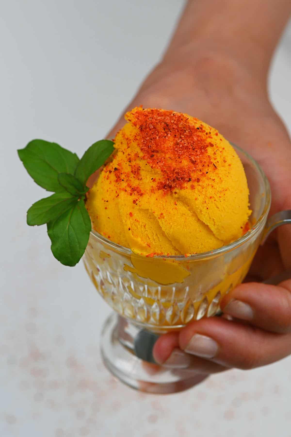 A serving of mango ice cream topped with mint and tajin