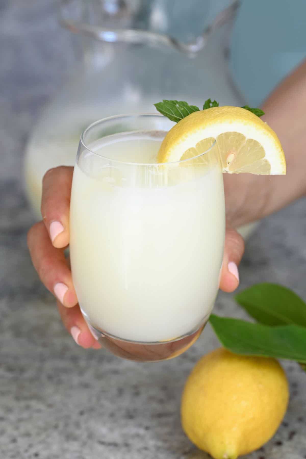 A hand holding a glass with creamy lemonade