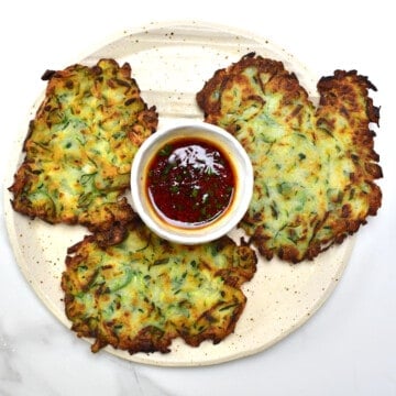 Three Korean Crispy Vegan Zucchini Fritters and dipping sauce on a plate