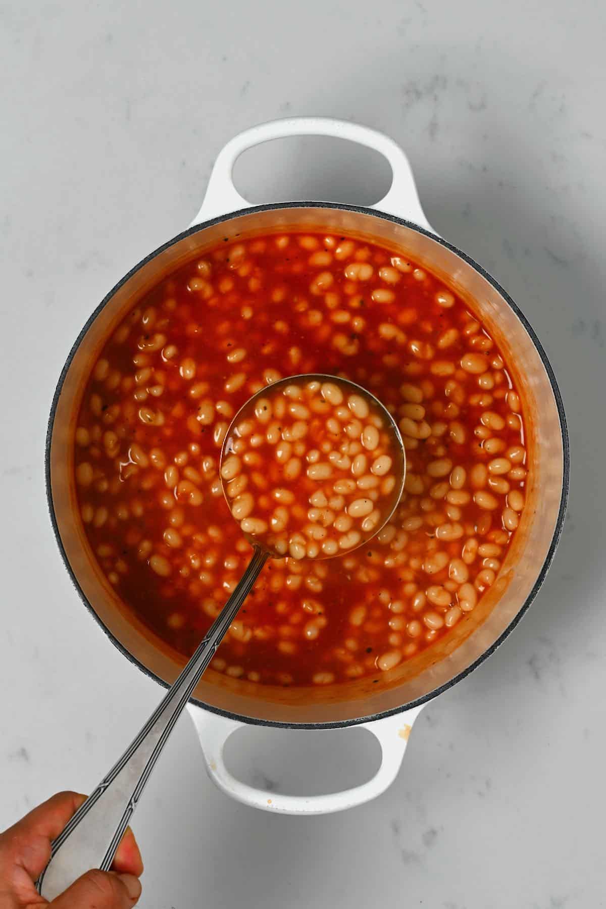 A ladle with homemade baked beans over a pot