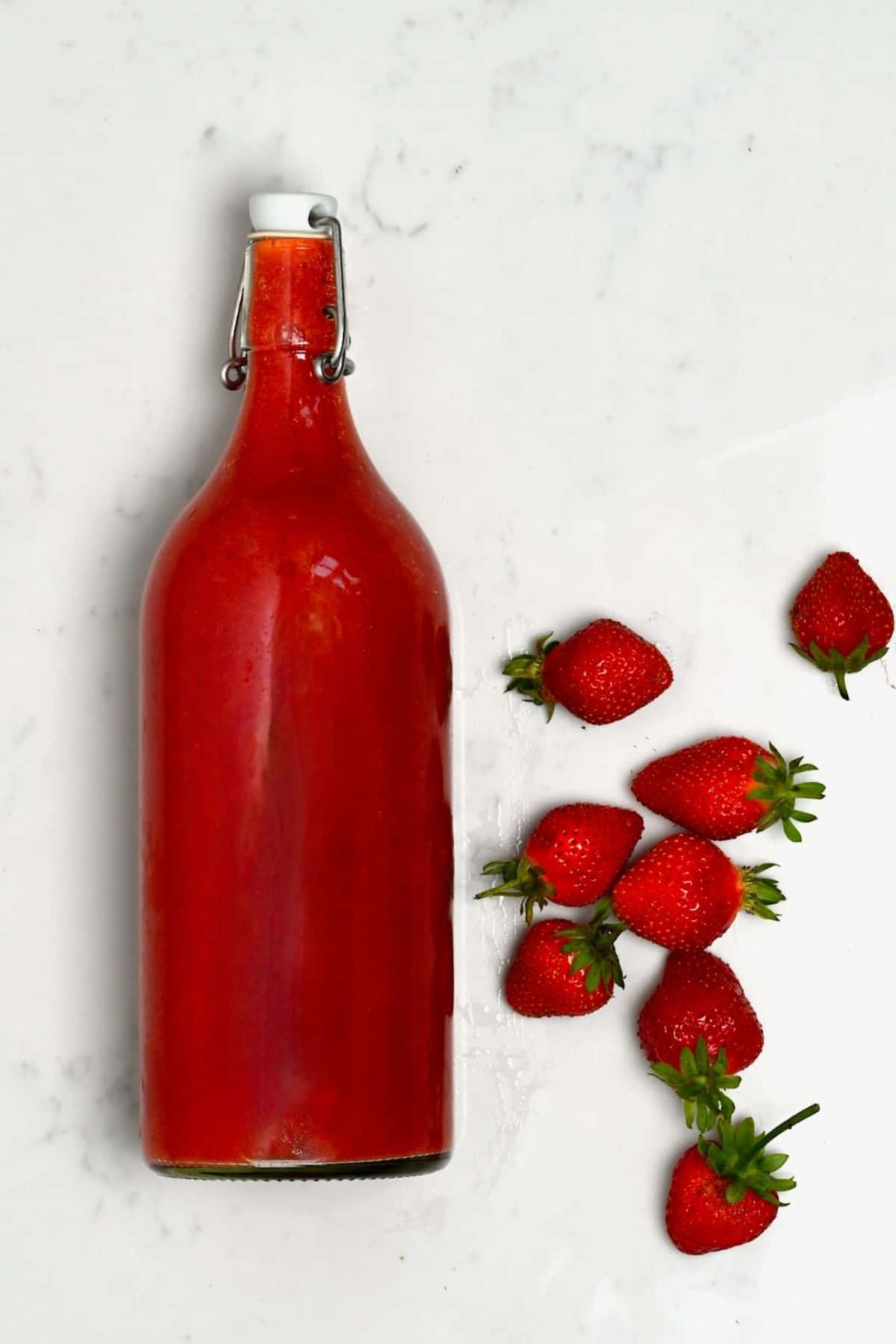 A bottle with strawberry juice and strawberries next to it