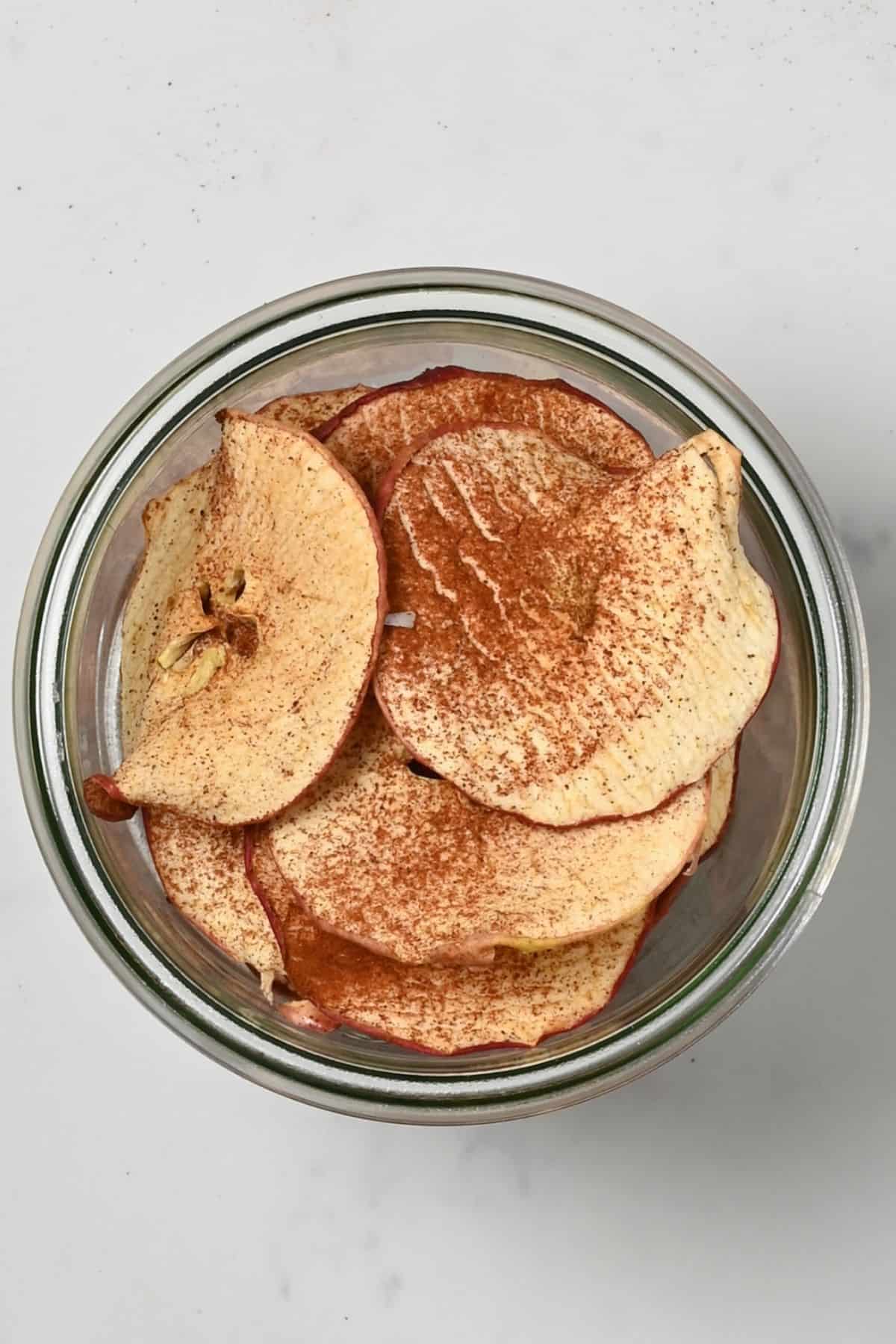 A jar with apple chips topped with cinnamon