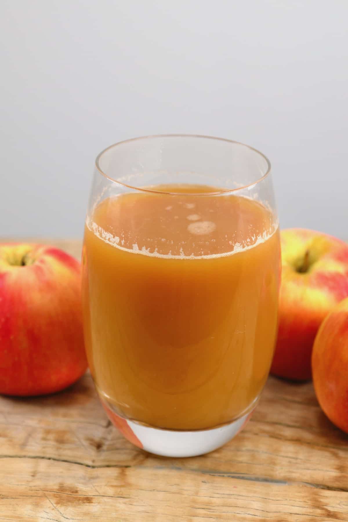 A glass of apple juice and three apples