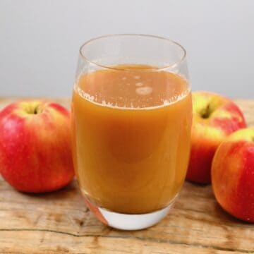 A glass of apple juice and three apples