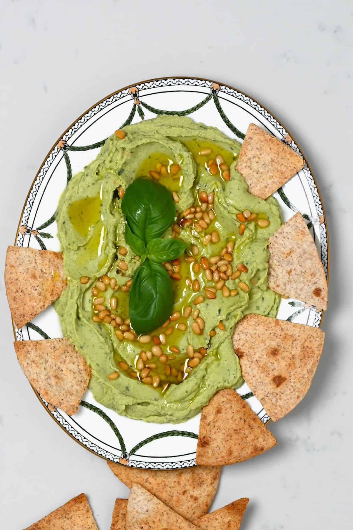 A plate with basil hummus and chips