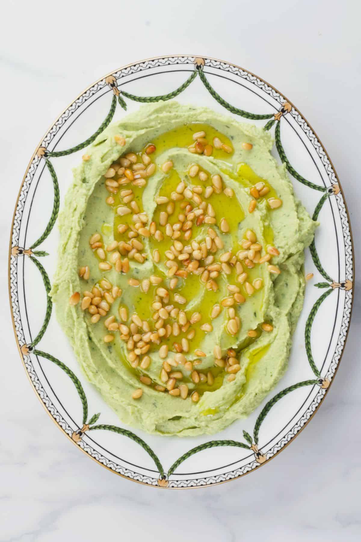 A plate with basil hummus topped with pine nuts