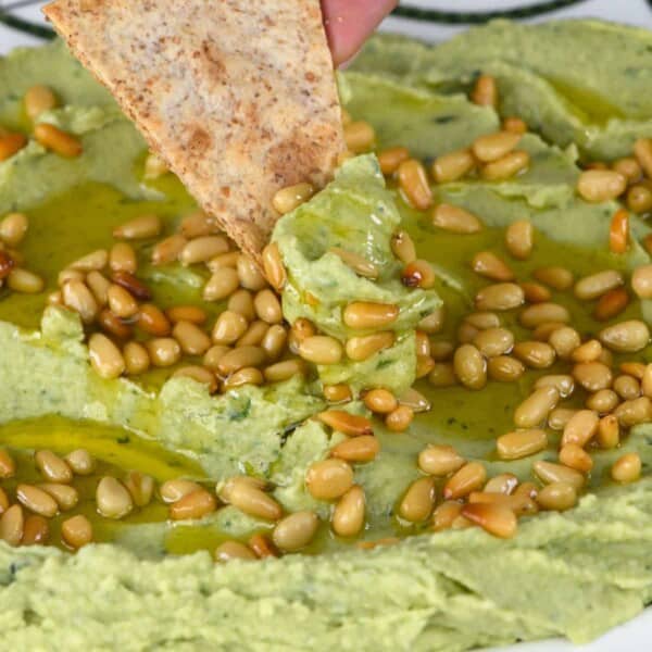 Scooping basil hummus with tortilla chip