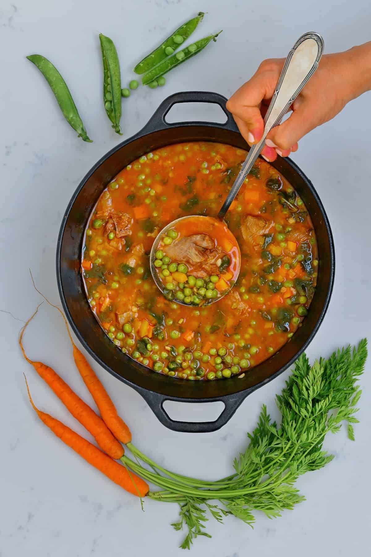 A saucepan with carrot pea stew and a ladle