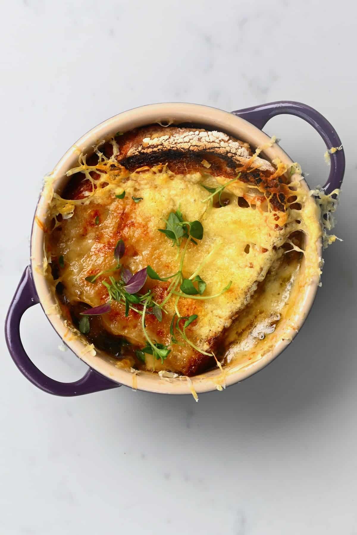 A bowl with onion soup topped with toasted bread and melted cheese